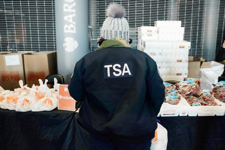 The back of a person in a TSA jacket as they look at packaged food on a table.